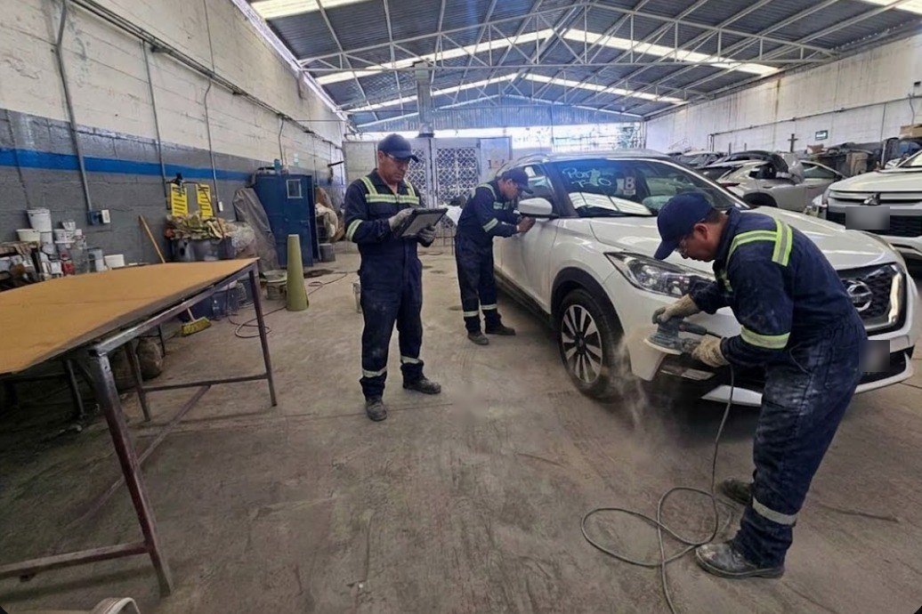 Técnicos con uniforme puliendo y revisando una camioneta blanca en la nave